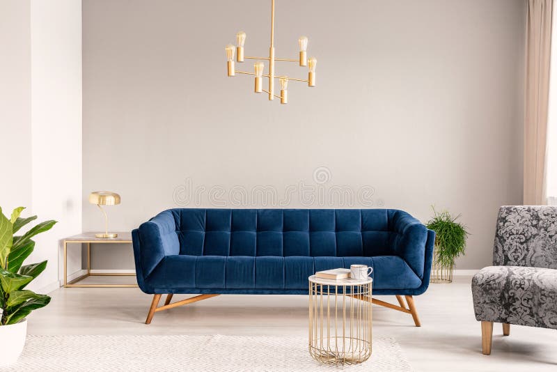 Gold lamp hanging above royal blue sofa in real photo of light grey sitting room interior with empty wall. Concept royalty free stock images