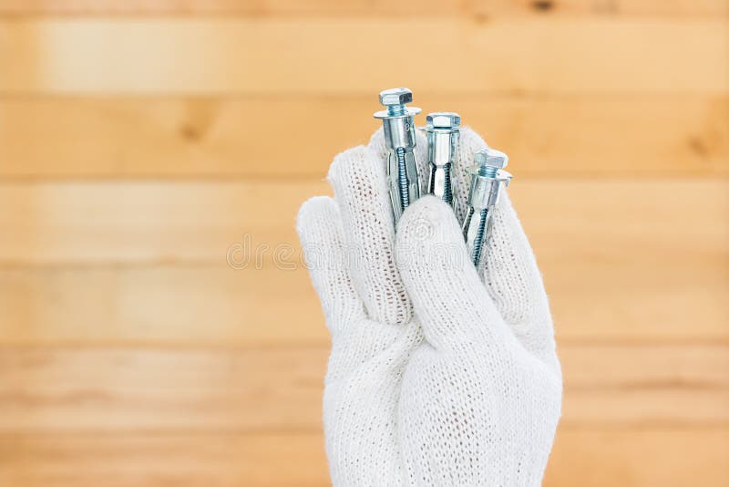 Hand in glove holding metal anchor bolts. Working hand in glove holding metal anchor bolts with wall wood background stock photo