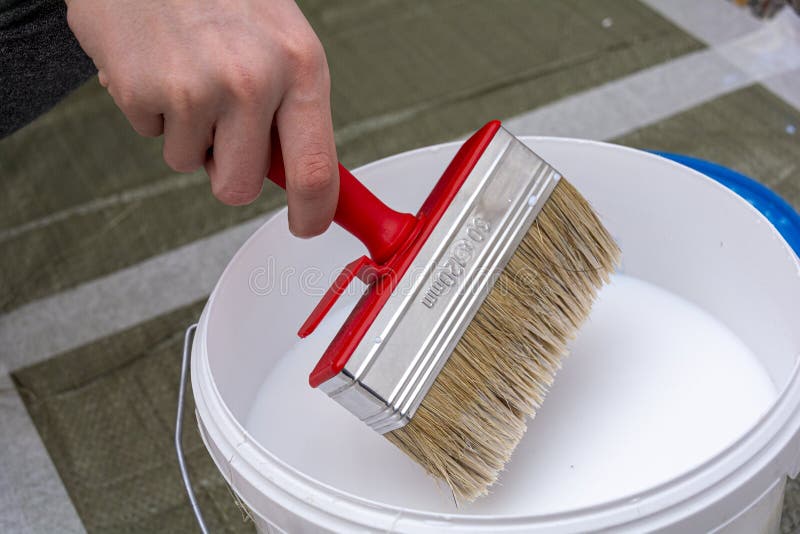 A hand holds a brush over a bucket of paint or primer. Concept: repair and wall decoration, repair royalty free stock images