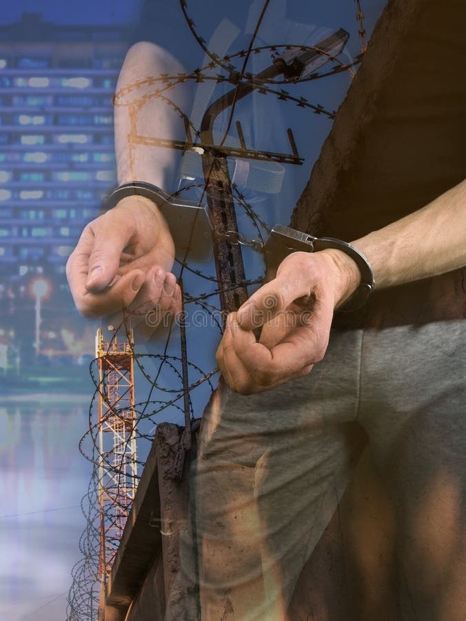 Handcuffs on the hands of a criminal against a background of a fence with barbed wire stock image