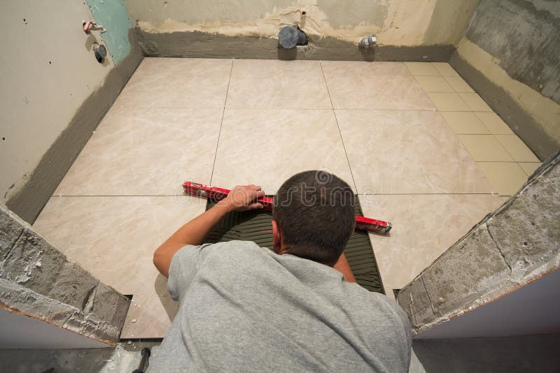 Home tiles improvement - handyman with level laying down tile floor. Renovation and construction concept. stock image