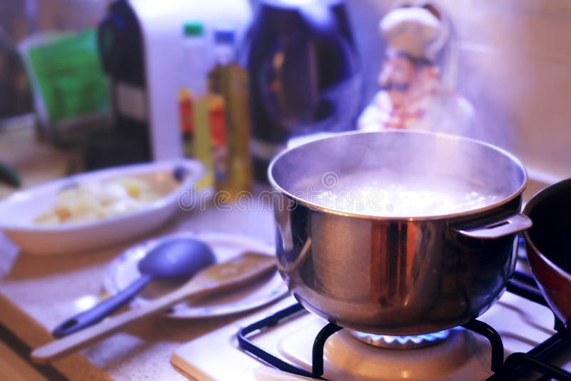 Hot cooking pot boiling on the stove in a cozy home like environment. In the background some cooking utensils and ingredients royalty free stock photos