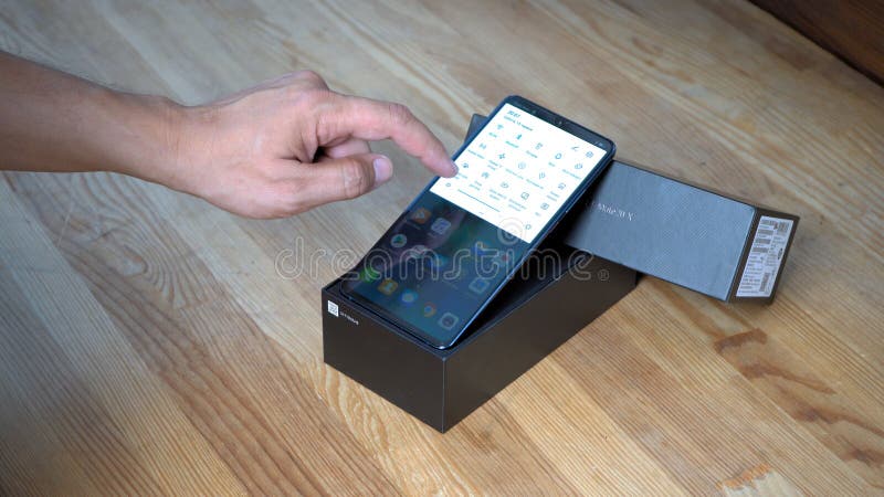 Huawei Mate 20 X smartphone screen. Phone with switched on screen lies in box on the wooden table. Man is clicking Huawei Mate 20 X smartphone display to show stock photo