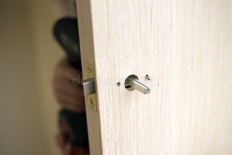Installation of door lock. Using a screwdriver to. Carpenter at lock installation with electric drill into wood door royalty free stock photography