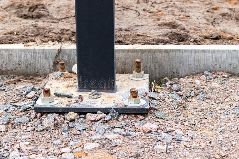 Installation of a lighting column or billboard with four anchor bolts on a track of a construction site covered with gravel. Near a concrete curb stock photos
