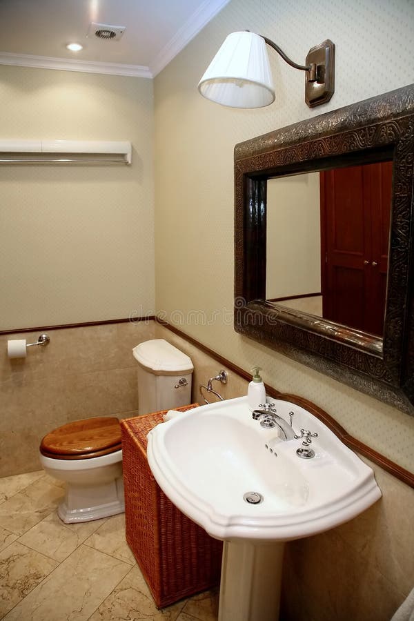 The interior of a rest room with toilet, sink and mirror in the gray-beige. The interior of a rest room in a grey-beige tones. The toilet tank, white sink, a stock photo