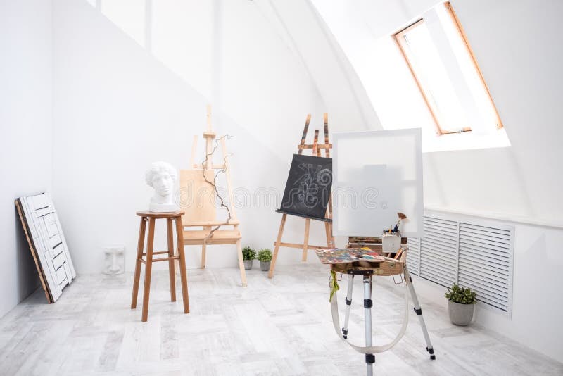 Interior of white studio of the artist, creative person. Easel, brushes, plaster head and figures. Attic, high ceilings. Daylight stock photo