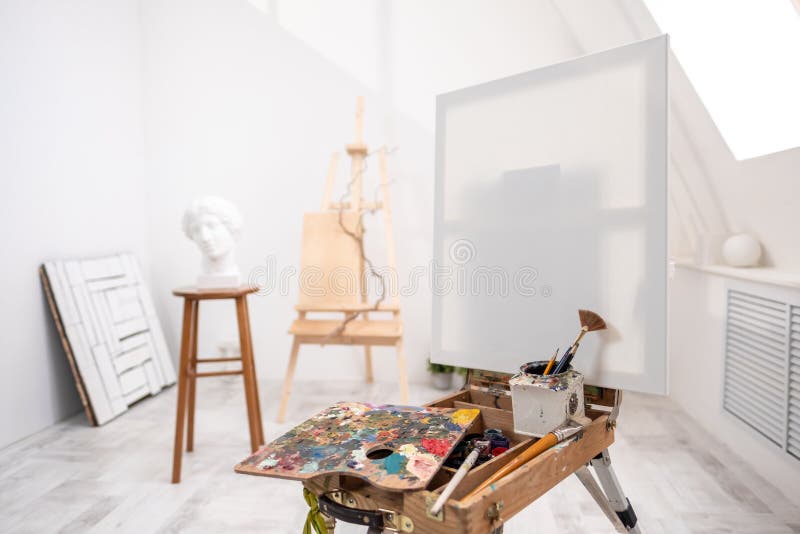 Interior of white studio of the artist, creative person. Easel, brushes, plaster head and figures. Attic, high ceilings. Daylight stock image