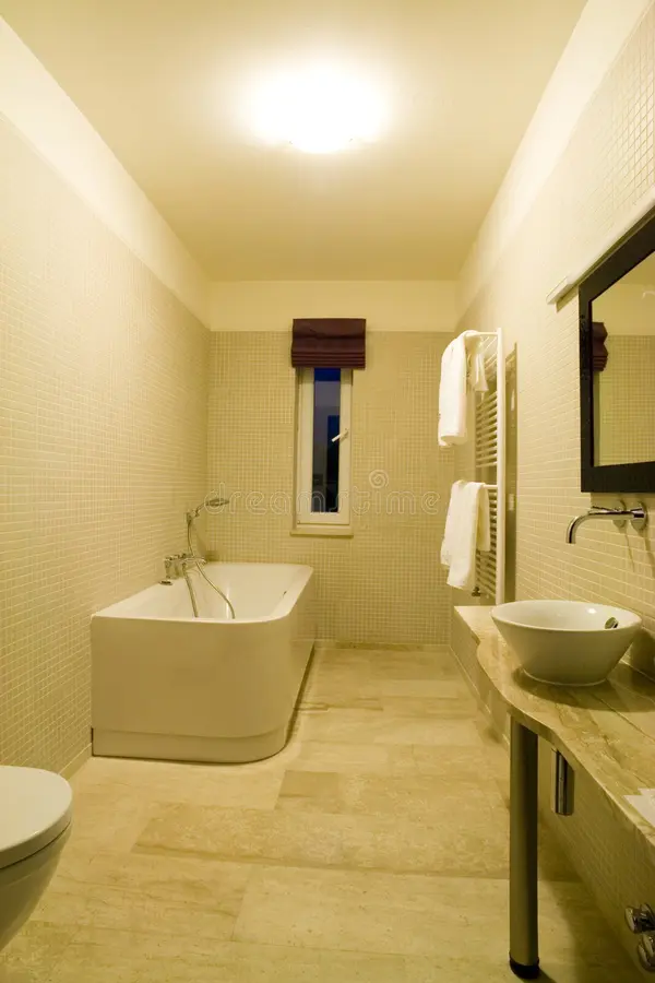 Interiors of a bathroom. A shot of the interiors of a modern and minimalist bathroom. Colour scheme is white and beige. Picture includes a bath tub, sink, mirror stock photography