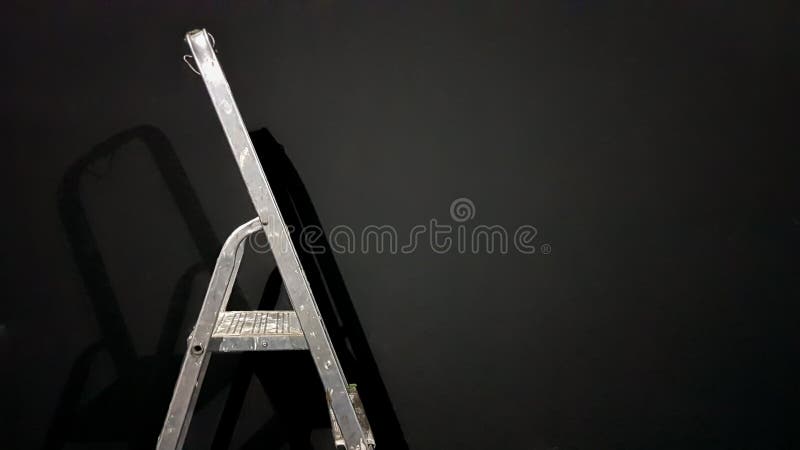 Iron step ladder against a gray wall. Preparing for home repairs. Old and dirty aluminum in an empty room, shadow. White gray stock image