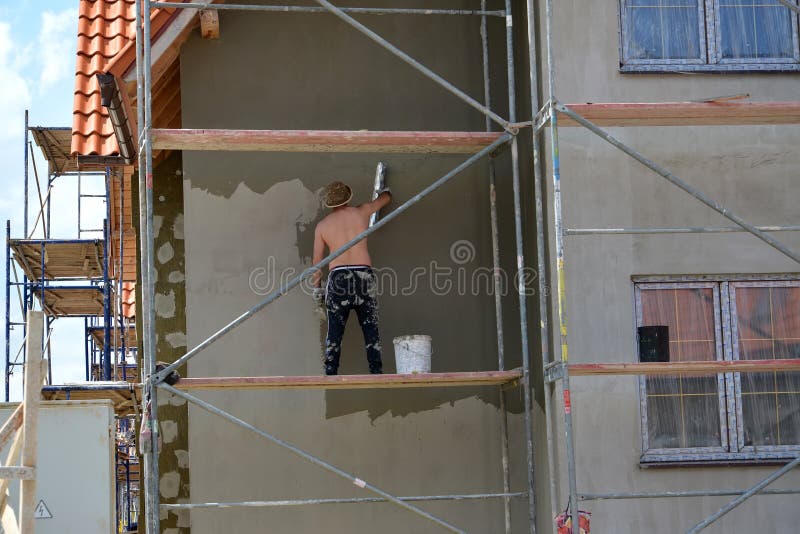 KALININGRAD REGION, RUSSIA. The worker plasters a cottage facade, standing on the construction woods. KALININGRAD REGION, RUSSIA - JUNE 01, 2016: The worker royalty free stock photos