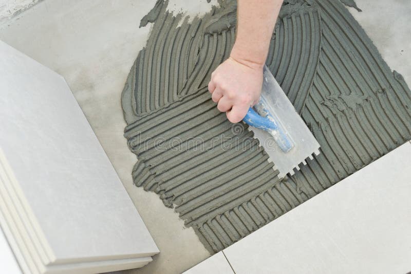 Laying Ceramic Tiles. Troweling mortar onto a concrete floor in preparation for laying white floor tile royalty free stock images