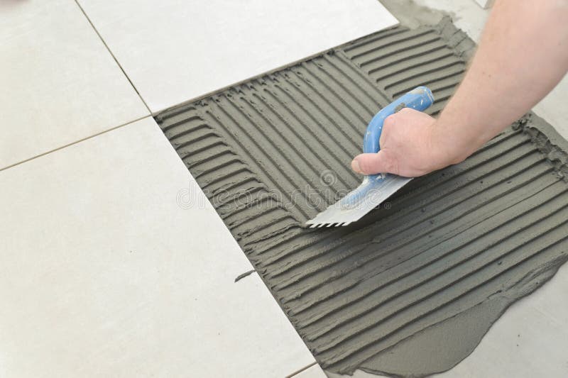 Laying Ceramic Tiles. Troweling mortar onto a concrete floor in preparation for laying white floor tile royalty free stock photos