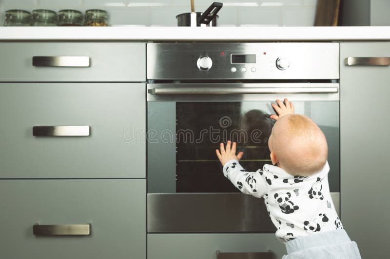 Little child playing with electric stove in the kitchen. Baby safety in kitchen. In a natural light stock images