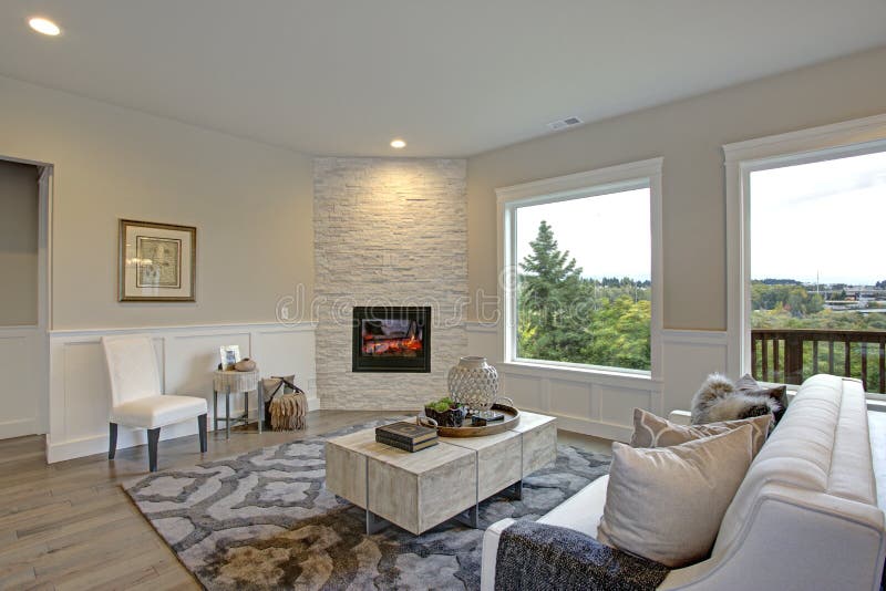 Luxury living room features corner stone fireplace. Relaxing white living room features corner stone fireplace lined with tan walls accented with lower wall stock image