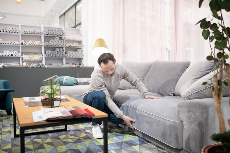 Man in light sweater and jeans examining the sofa. Before buying. Man in light sweater and jeans examining the sofa royalty free stock images