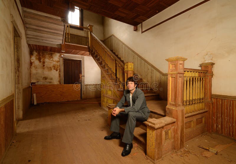 Man Sitting on Stairs in an Old House. Msn in suit sitting on the stairs of an old abandoned house royalty free stock images