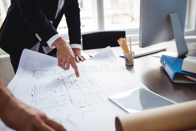 Manle interior designer discussing blueprint with coworker. Midsection of male interior designer discussing blueprint with male coworker in office stock photo