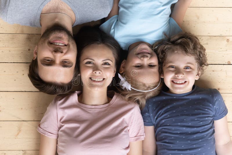 Top view parents little kids lying on wooden warm floor. Married couple and lovable kids smile lying down together on wooden warm floor with underfloor heating royalty free stock photography