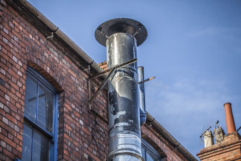 Metal chimney on the old brick house. Ventilation tube chimney on the red brick house. Blue sky in the background. royalty free stock photo