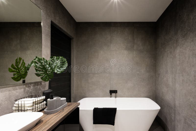 Modern bathroom wall made in dark color tiles. Which covered the bathtub and towels near the fancy plant stock photos