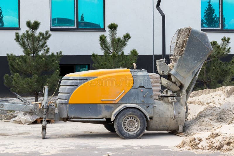 Modern concrete screed pump at a construction site next to a pile of sand, a building and pine trees.  royalty free stock photography