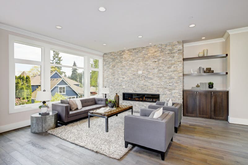 Modern great room with a floor to ceiling stone fireplace. Modern great room features a floor to ceiling stone fireplace, gray tufted sofa paired with two gray royalty free stock images