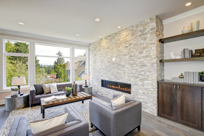 Modern great room with a floor to ceiling stone fireplace. Modern great room features a floor to ceiling stone fireplace, gray tufted sofa paired with two gray royalty free stock photos