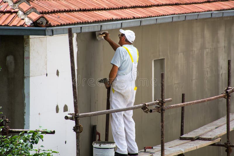 Worker spreading mortar over styrofoam insulation and mesh with trowel on house facade. Nis, Serbia - June 16, 2018: Male worker spreading mortar over styrofoam stock image