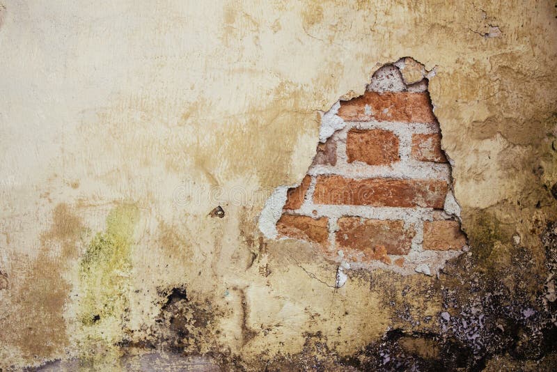 Old dirty and grungy plastered wall facade of an abandoned house with a hole showing the underlying red bricks. Below the cement royalty free stock photography