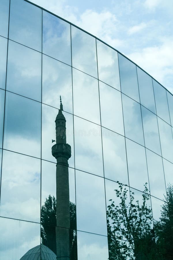 Old mosque with its typical minaret mirroring and reflecting on a modern office building in the city center of Prishtina, Kosovo stock photos
