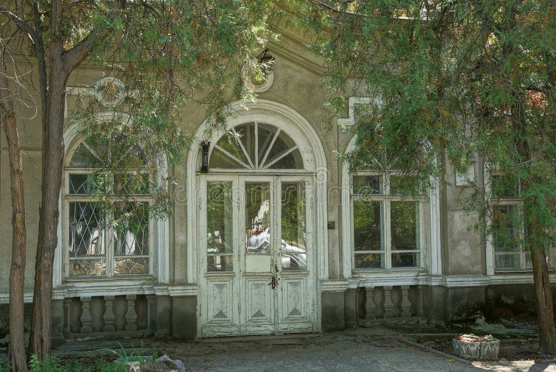 Old white door made of wooden boards and glass on a gray wall with windows stock photo