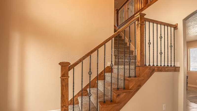 Panorama frame Carpeted stairs with wood handrail and metal railing inside an empty new home. Beige wall, shiny floor, window with blinds, and arched doorway royalty free stock images