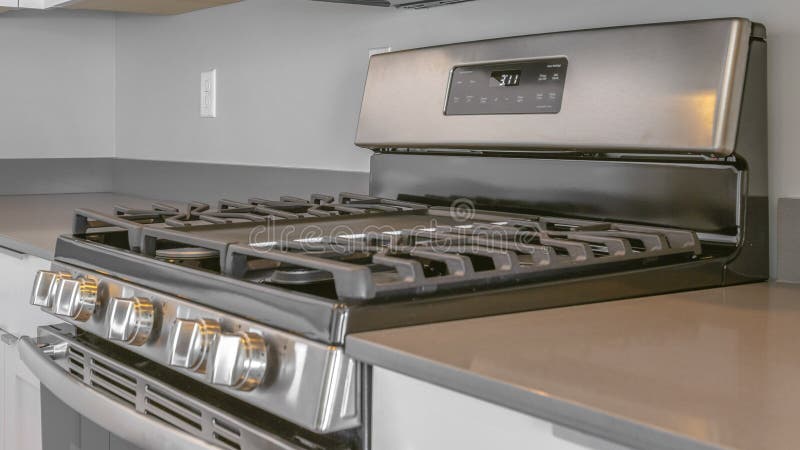 Panorama frame Range with cooktop and oven inside the modern kitchen of a new house. A microwave is mounted on the wall above the shiny cooking range stock photography