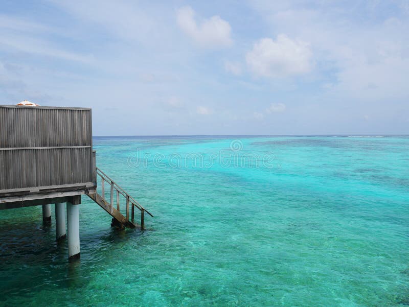 Part of Maldives water villa room in an island resort, seeing wood stairs down from balcony to ocean floor. Underwater reefs can also be seen under clear blue royalty free stock photos