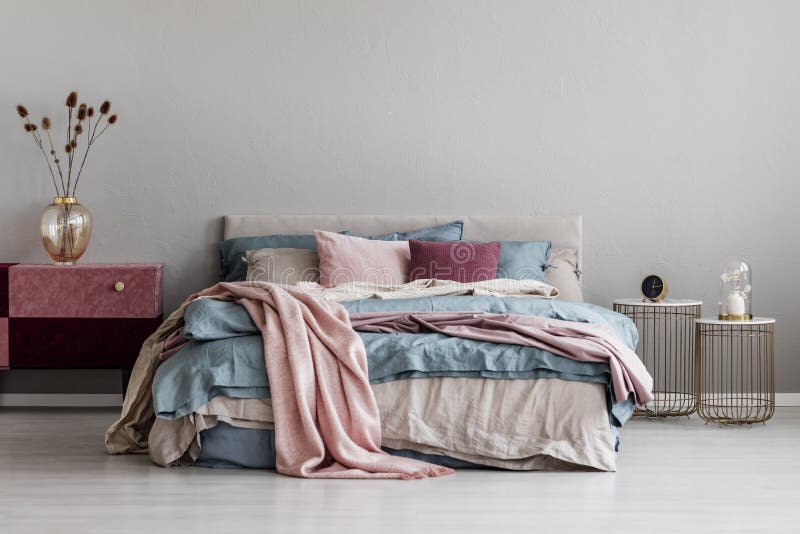 Pastel pink, beige and blue bedding on king size bed in trendy bedroom interior, copy space on empty grey wall. Pastel pink, beige and blue bedding on king size royalty free stock photo