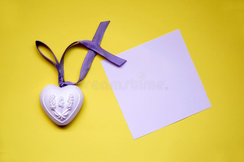 Plaster heart with embossed lavender and a white sheet of paper on a yellow background. Small souvenir heart with purple ribbon. Top view, mock up, flat lay stock photo