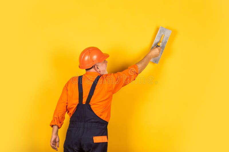 Plaster trowel spatula on yellow drywall plasterboard. Plasterer in working uniform plastering wall indoor. man with. Spatula. process of applying layer of stock photography
