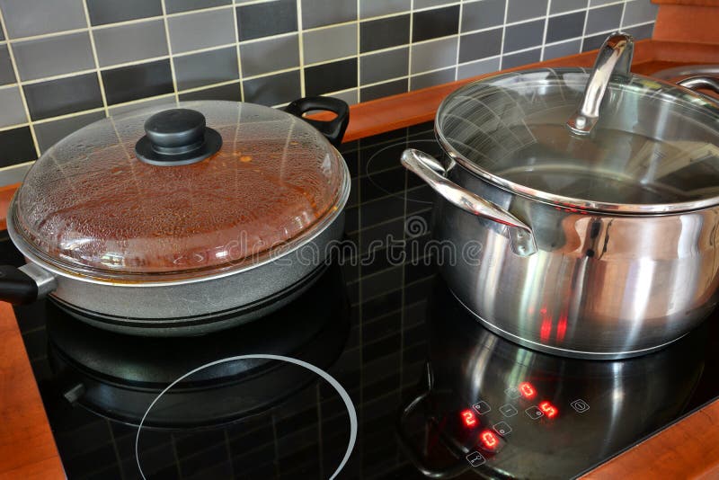 Pot and pan on kitchen induction stove. Black kitchen induction stove with stainless steel pot and pan. Cooking in pots on kitchen stove with modern tiling stock photography