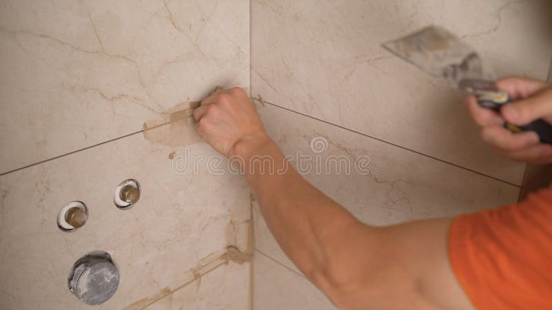 Master tiler glues wall white ceramic tiles. The process of grouting the joint between tiles in the bathroom. The master glues the. The process of grouting the stock photos