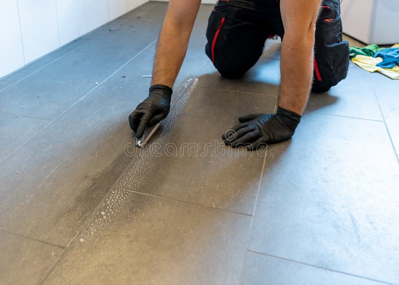 Professional cleaner cleaning grout with a brush blade and foamy soap on a gray tiled bathroom floor. A professional cleaner cleaning grout with a brush blade royalty free stock photo