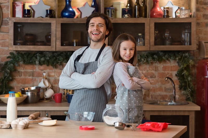 Ready For Baking. Dad And Little Daughter Posing In Kitchen Wearing Aprons royalty free stock photos