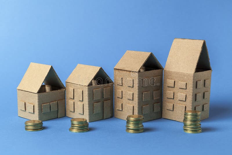 Real estate and money. Cardboard houses and coins on a blue background. Growth in rental prices. Investing in building.  royalty free stock photography