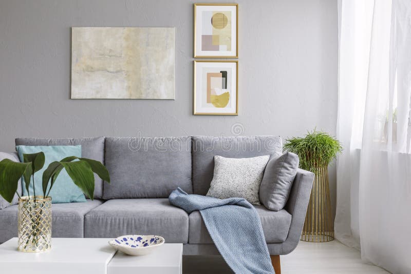 Real photo of a grey sofa standing in a stylish living room interior behind a white table with leaves and in front of a grey wall stock image