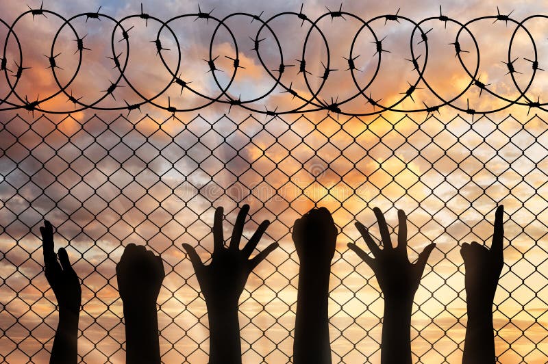 Refugees hands silhouette near the fence of barbed wire. stock photos