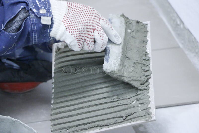 Repair - interior decoration. Laying of floor ceramic tiles. Men`s hands tiler in gloves with spatula spread cement mortar on royalty free stock photography