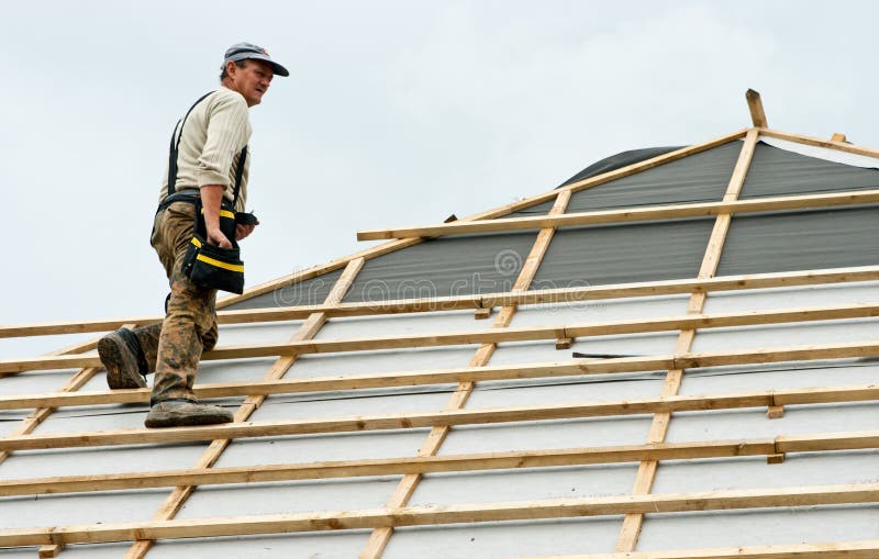 Roofer at work on roof. Roofer holding tool bag standing on roof also showing insulation and wooden battens in preparation for tiling stock photography