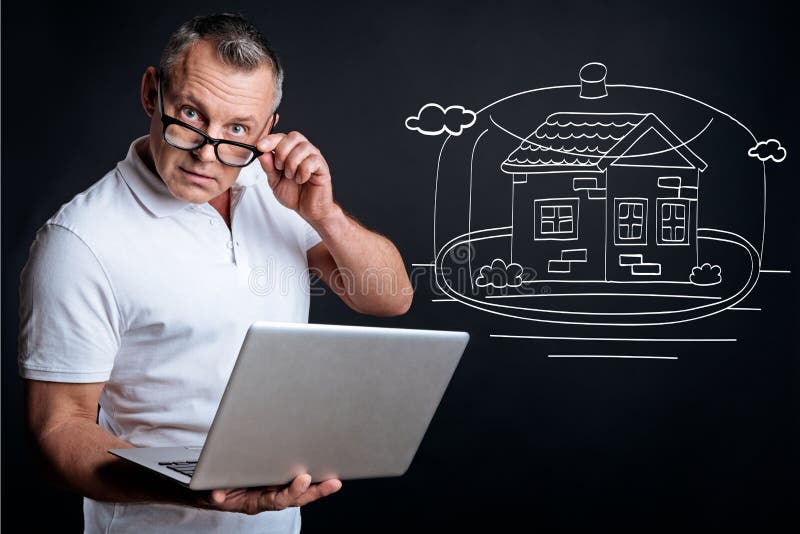 Serious man planning buying the house. Think it over in advance. Serious adult businessman holding laptop and looking at you while planning buying new house royalty free stock photos