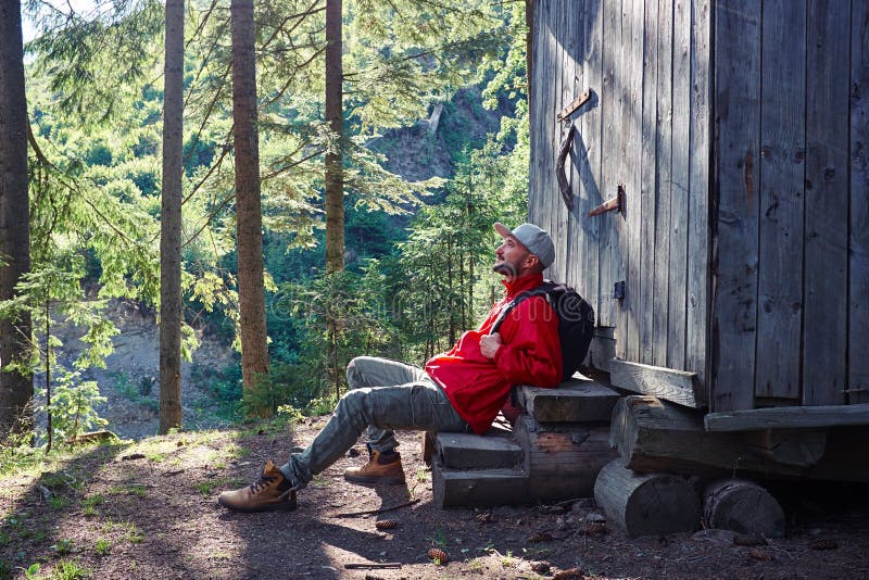 Inspired man sitting on stairs of wooden house. Side view of young bearded man sitting on stairs of wooden house in the morning royalty free stock photo