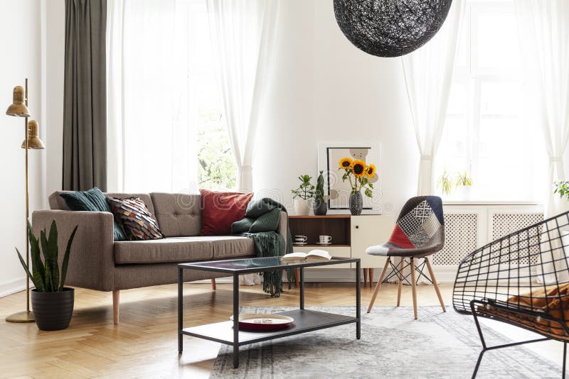 Simple brown sofa with cushions in an eclectic, white living room interior with natural light coming through big windows. Concept stock photos